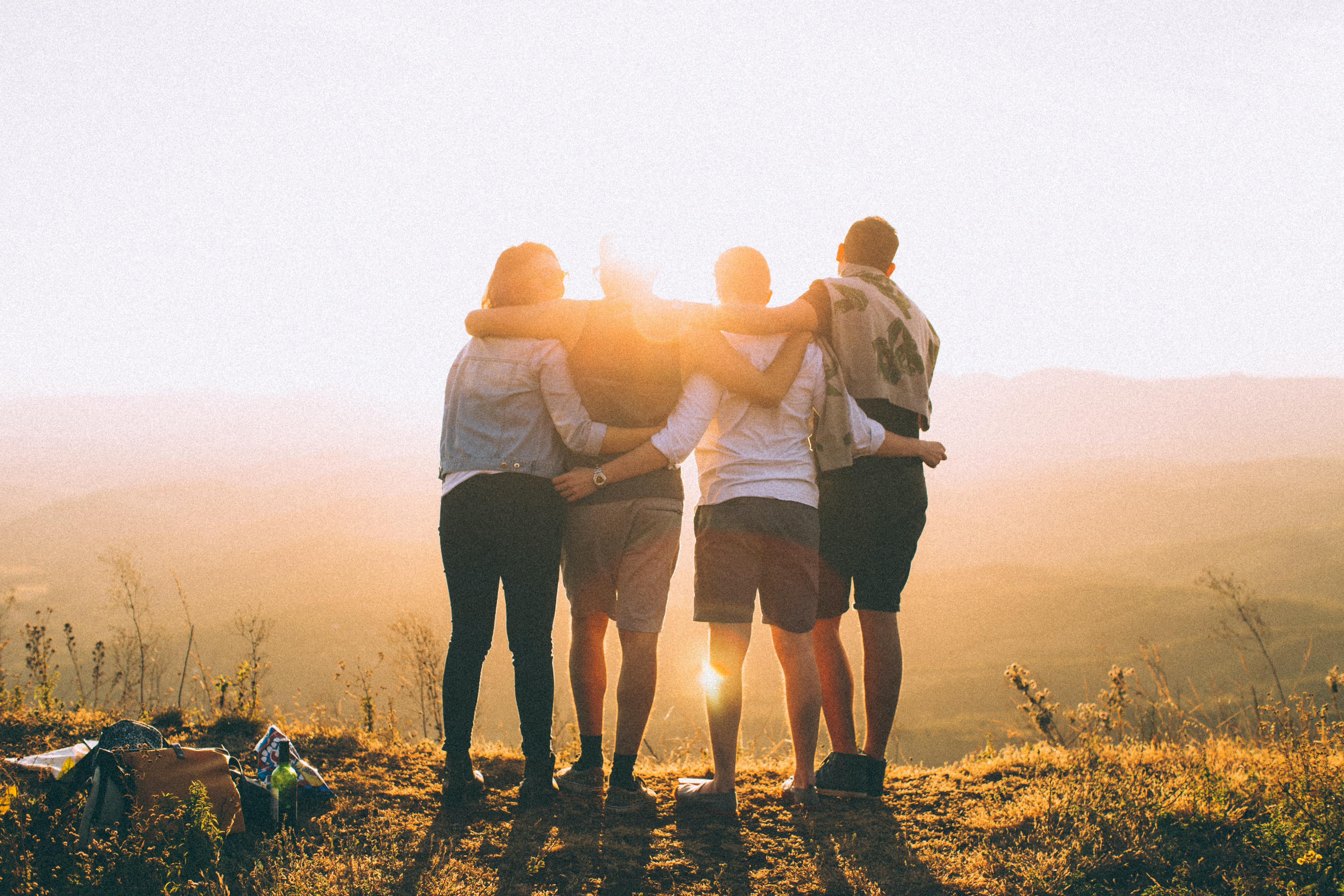 Four people on a hilltop watching the sunset, though it looks more like they're staring directly at the full sun since it's pretty far from the horizon